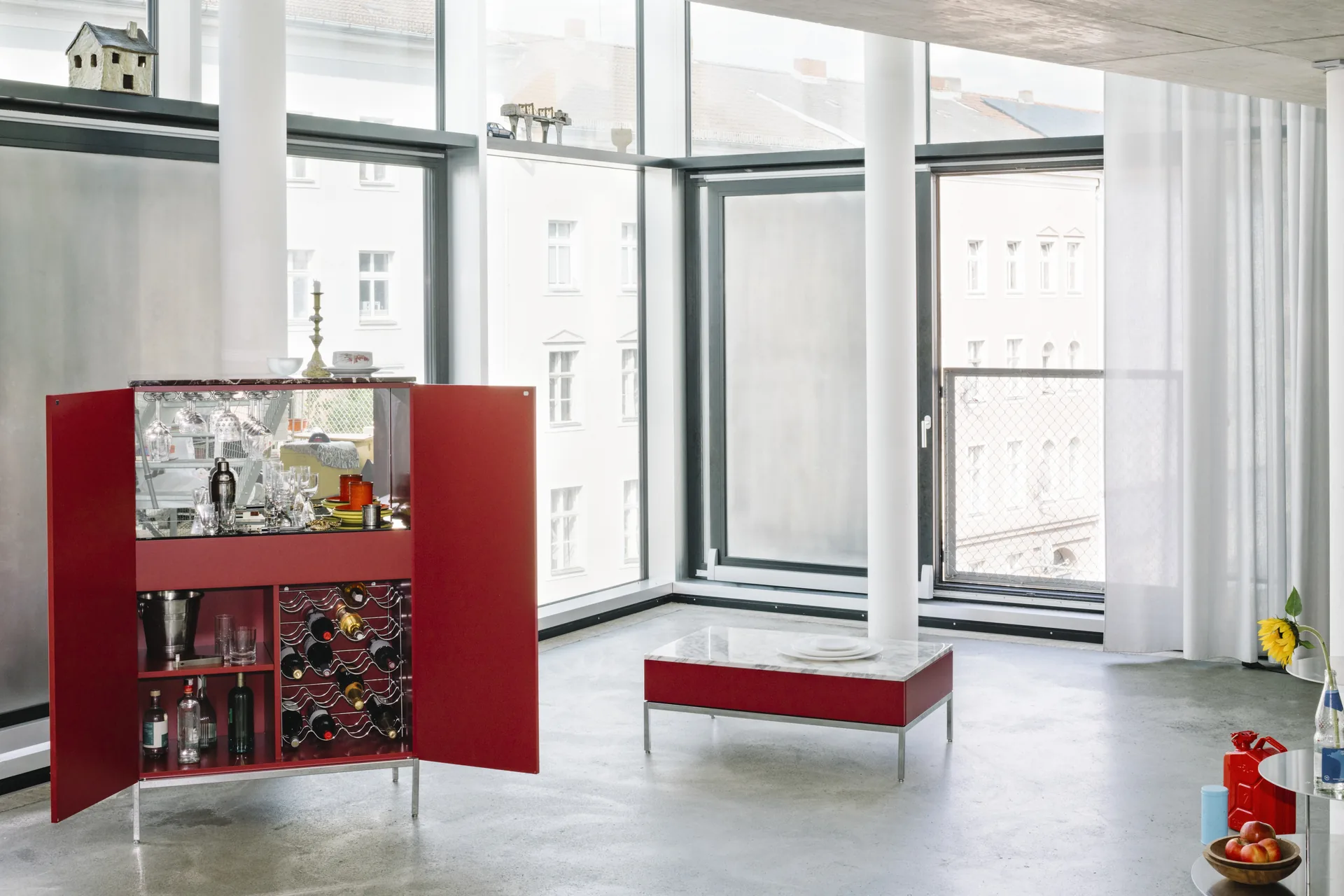 Mueble bar Knoll Chermayeff Storage lacado en rojo, abierto, con copas y botellero en un loft