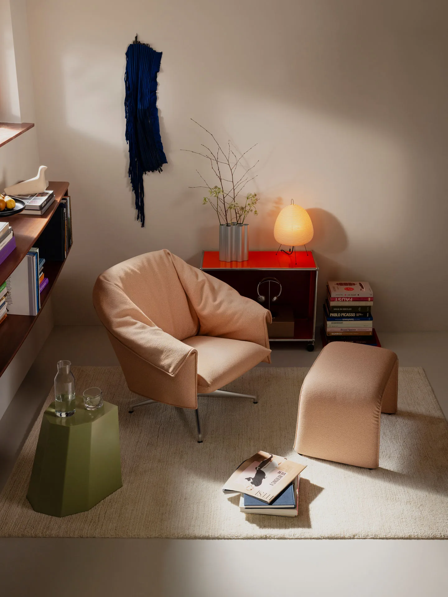 Butaca Vitra Bascule en tela color melocotón con otomana junto a un aparador y una lámpara