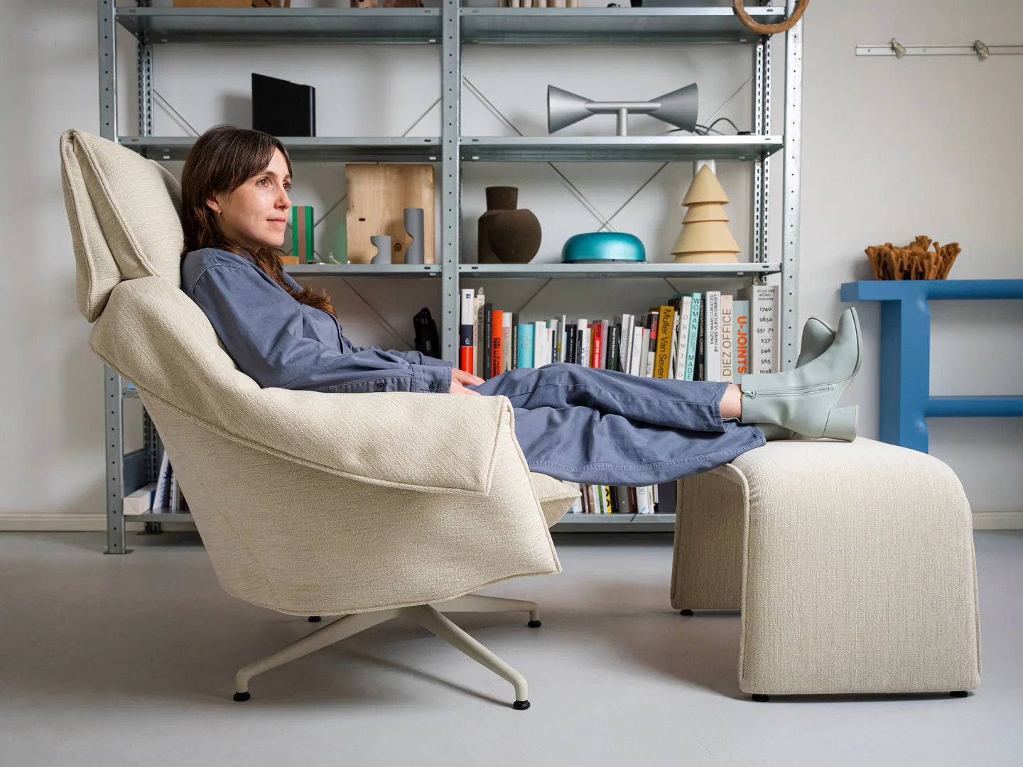 Butaca Vitra Bascule Highback con otomana, reclinada, en una habitación con estantería abierta
